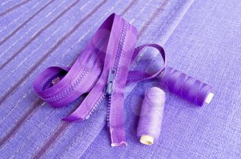 Locking zipper and two reels of thread on the purple plain and striped fabrics