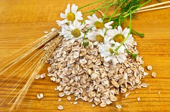 Rye flakes, a bouquet of daisies and stalks of rye on a wooden board