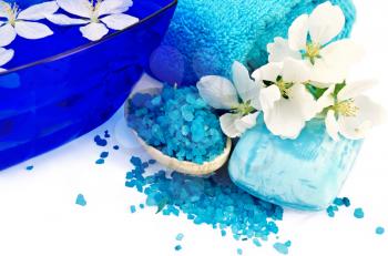 The blue salt in a wooden spoon, soap, towel, a bowl of water and white flowers of apple isolated on white background
