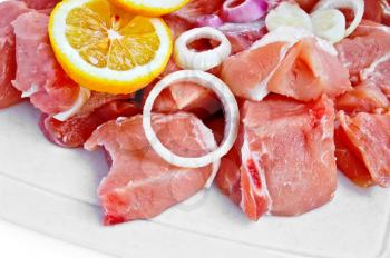 Sliced pork with onion and lemon lobule on a plastic board isolated on white background