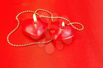 Two red candles in the shape of a heart with golden decorations on a red silk
