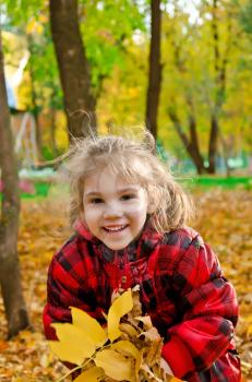 Little girl with a bunch of yellow leaves on a background of trees and yellow foliage