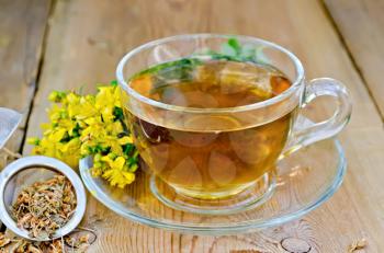 Tea in a glass cup, a metal filter for tea with dried flowers tutsan, Hypericum fresh flowers on the background of wooden boards