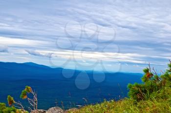 A view of the chain of mountain peaks of the Northern Urals (Kosva), sky and clouds, green grass and small trees cedar
