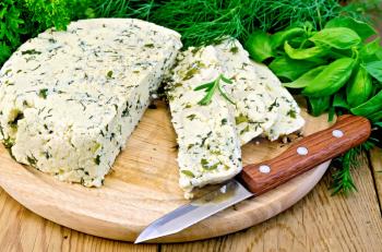 Homemade round cheese with herbs and spices cut into slices, knife on a wooden board