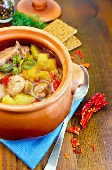 Roast with chicken meat, potatoes and peppers in a clay pot, napkin, spoon, crispbreads, dill on a wooden board