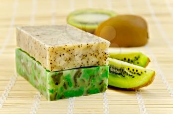 Two green homemade soaps, kiwi slices on a bamboo napkin