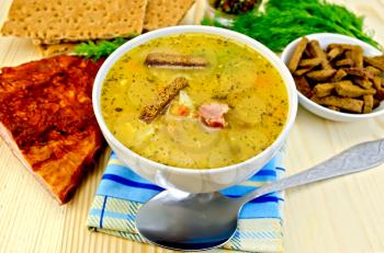 Pea soup in a bowl, rye crackers on a plate, spoon, pepper, crispbread, cloth, bacon, dill against a wooden board
