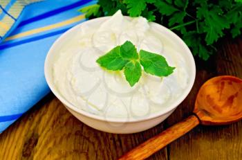 Thick yogurt in a white bowl, parsley, spoon, napkin, mint on a wooden board