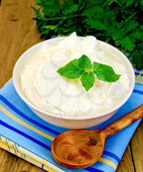 Thick yogurt in a white bowl, parsley, spoon, napkin, mint on the background of wooden boards