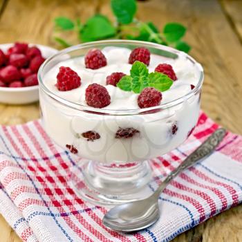 Thick yogurt in glass with raspberries and spoon on a napkin, raspberries in the bowl, mint on the background of wooden boards