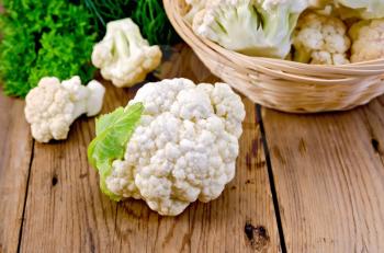 Cauliflower on a table and in a wicker basket, dill, parsley on wooden board