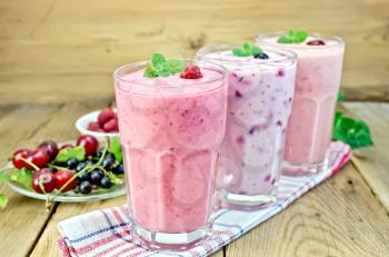 Milkshakes with black currant, cherry, raspberry in glass on the background of wooden boards