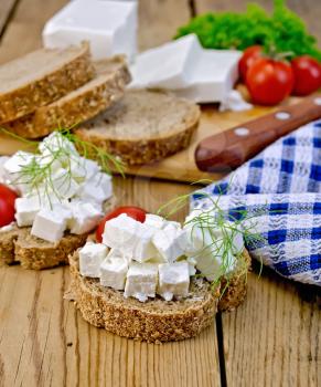 Slices of bread with feta cheese, tomato and dill, napkin on wooden board