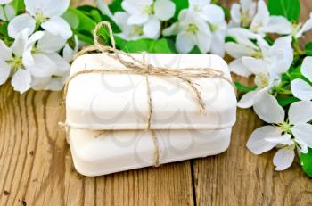 Two bars of soap with white flowers of apple trees on the background of wooden boards