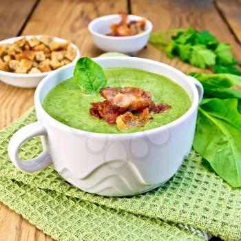 Green soup puree in a white bowl with leaf spinach and grilled meat on a napkin, crackers on a wooden boards background
