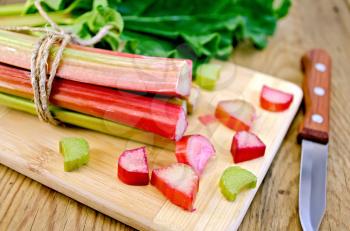 Bundle of stalks rhubarb, rhubarb pieces with a sheet, a knife on a wooden boards background