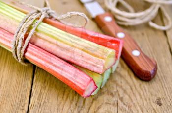 Bundle of stalks of rhubarb with a knife and a coil of rope on the background of wooden boards