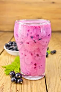 Milkshake with black currants in a glass, currants against the background of wooden boards