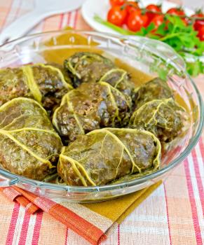 Stuffed cabbage with meat and rhubarb leaves in a glass dish, parsley, tomatoes on a cloth background