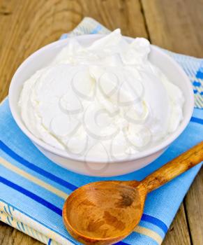 Thick yogurt in a white bowl, spoon, napkin on a wooden boards background