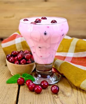 Thick yogurt in a glass goblet with cranberries, napkin, cranberries in a bowl, mint on a wooden boards background