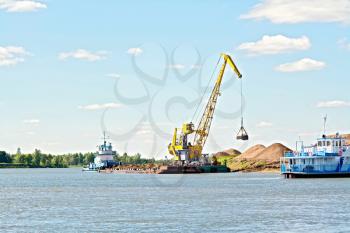 Loading sand with the help of a crane on a barge on the water and sky background of yellow sand. River White, Russia