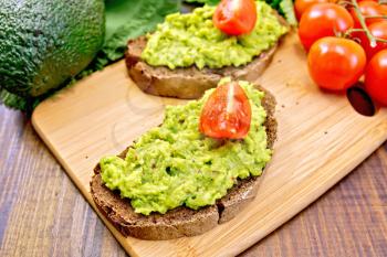 Two slices of rye bread with tomato and guakomole, napkin, avocado on a wooden boards background