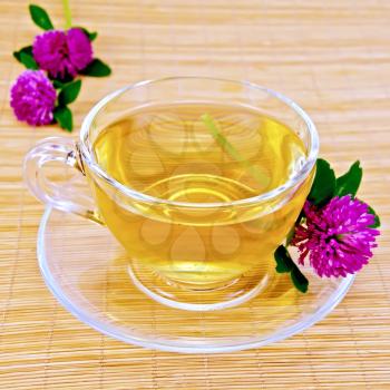 Herbal tea with flowers of clover in a glass cup on a bamboo napkin