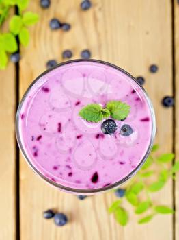 Milkshake with blueberries in a glass, berries and leaves of blueberries on a wooden boards background top
