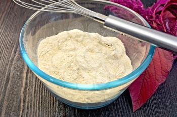 Amaranth flour in a glass bowl with mixer, purple amaranth flower on the background of wooden boards