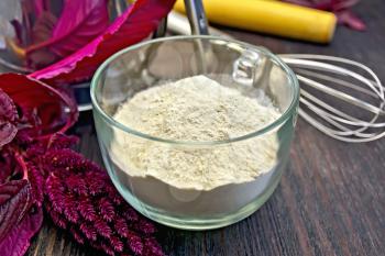 Amaranth flour in a glass cup, mixer, rolling pin, sieve and purple amaranth flower on the background of wooden boards