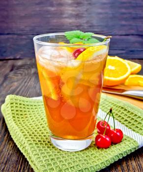 Lemonade in a glass with a cherry, lemon and orange, mint on green napkin on a dark wooden board