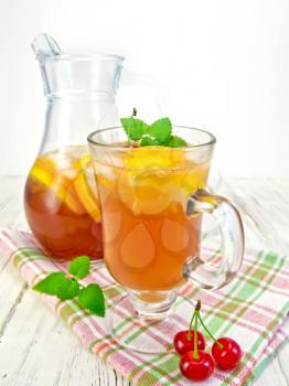 Lemonade in a wineglass and jug with a cherry, lemon and orange, mint on a napkin on a wooden boards background