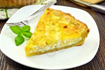 Tart with cheese, leek and sour cream and egg cream in a white dish, cheese and knife on a wooden boards background