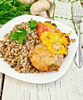 Cutlet of turkey meat with buckwheat, mushrooms, tomatoes and peppers in the dish, parsley, a towel and a fork on the background of wooden boards