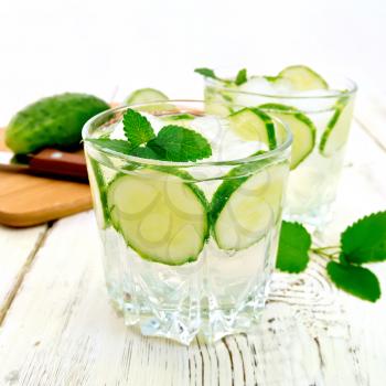 Lemonade with cucumber and mint in two glasses, a knife, a cucumber on the background light wooden boards