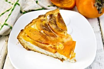 Sweet pie with curd and persimmons in a white plate, kitchen towel on a background of wooden boards