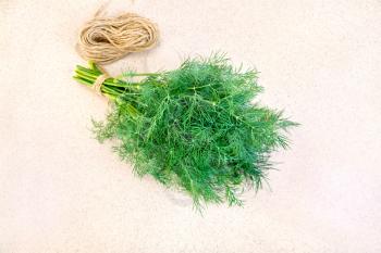 A bunch of dill and a skein of twine on a background of a granite table top