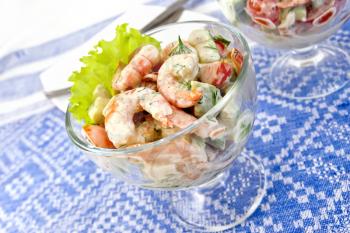 Salad with shrimp, avocado, tomato and mayonnaise, green salad in a glass goblet on a background of blue linen tablecloth