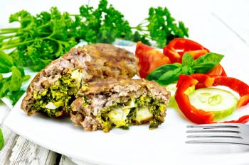 Cutlets stuffed with spinach and egg, slices of tomato, cucumber and pepper in a dish on a towel, basil and parsley on a wooden board background
