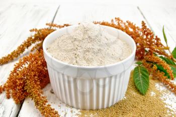 Amaranth flour in a bowl, seeds scattered on the table, brown flower with leaves on the background of wooden boards