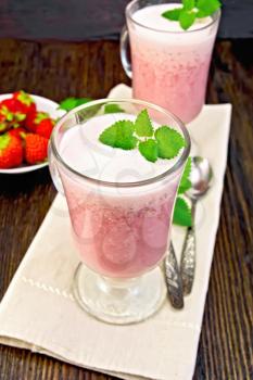 Strawberry soup in two glass goblets with mint, spoon on a napkin, berries in a bowl on a wooden boards background