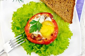 Scrambled eggs with ham and mushrooms in a tomato on a green lettuce in the plate, bread, fork and a napkin on a background of wooden boards on top