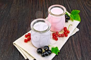 Milk cocktail with black and red currants in glass jars on a towel with berries on a wooden board background