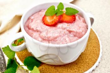 Strawberry soup with berries and mint in a bowl on a stand, a towel and a spoon on a background of stone table