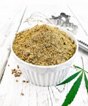 Hemp flour in a white bowl, mixer and cookie cutters, cannabis leaves on the background wooden boards