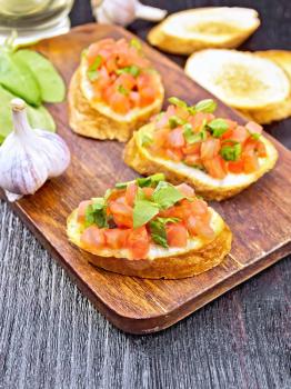 Bruschetta with tomato, basil and spinach on a plate, vegetable oil in a decanter, garlic on wooden board background