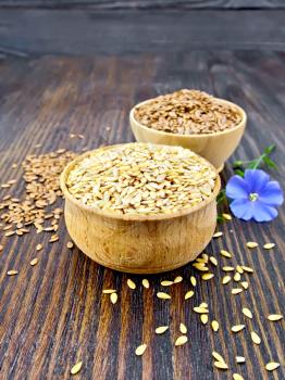 Linen seeds are white and brown in two bowls and a blue flax flower on the background of a dark wooden board