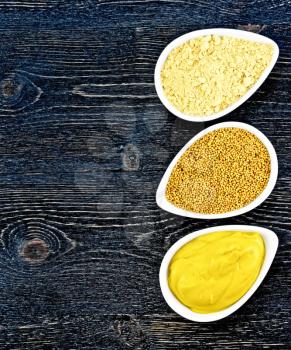 Mustard sauce, seeds and mustard powder in three saucepans on the right against a black wooden board on top